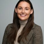 Woman with brown hair posing in front of a gray background