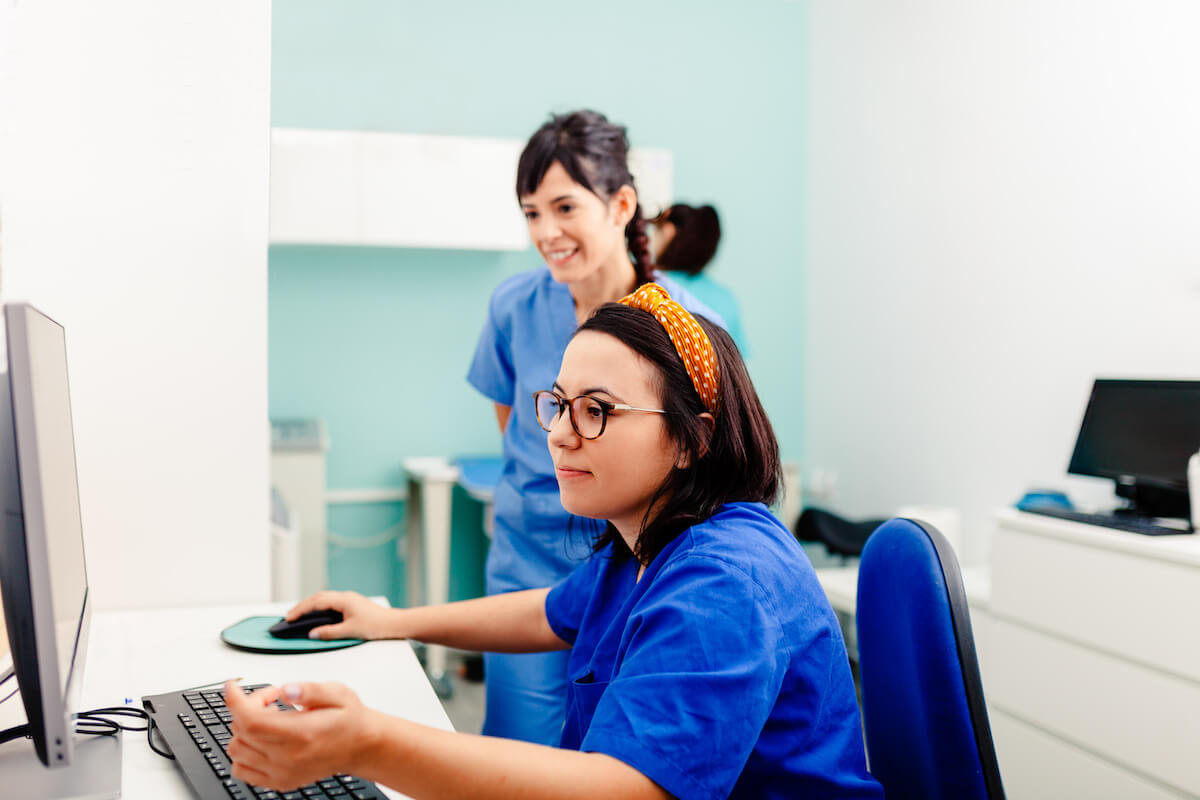 Nurse with glasses showing graduate nurse how to use computer system.