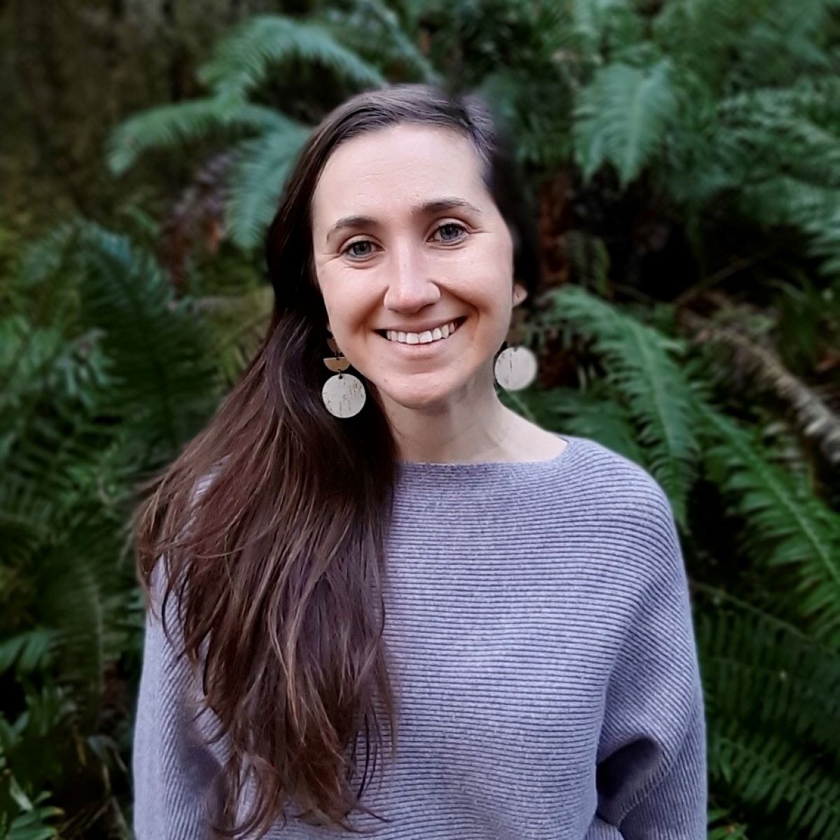 Content creator standing in front of green trees smiling for camera