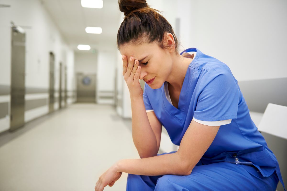 Nurse experiencing nurse burnout and sitting down while holding her head