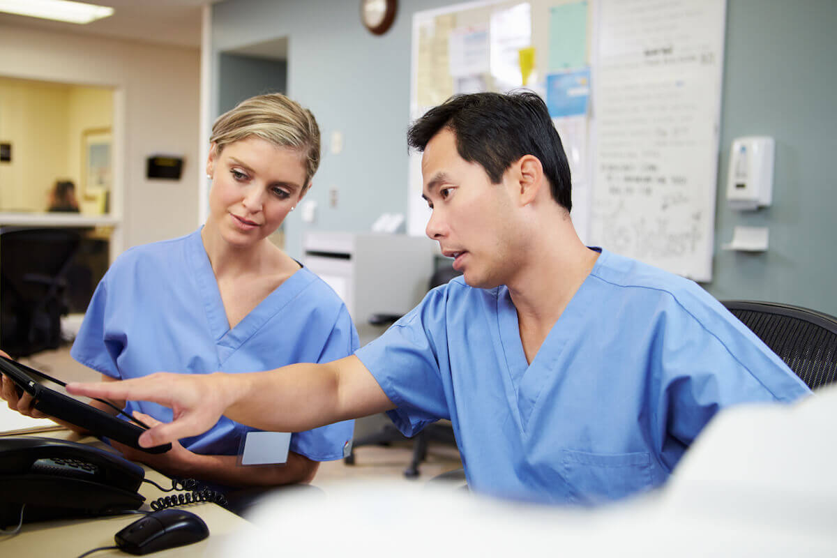 Male and female nurse sitting behind desk and working on computer together.