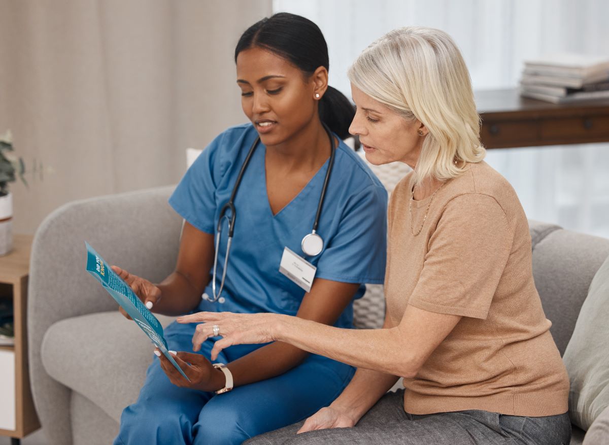 An RN sits and shows something on her tablet to a patient.