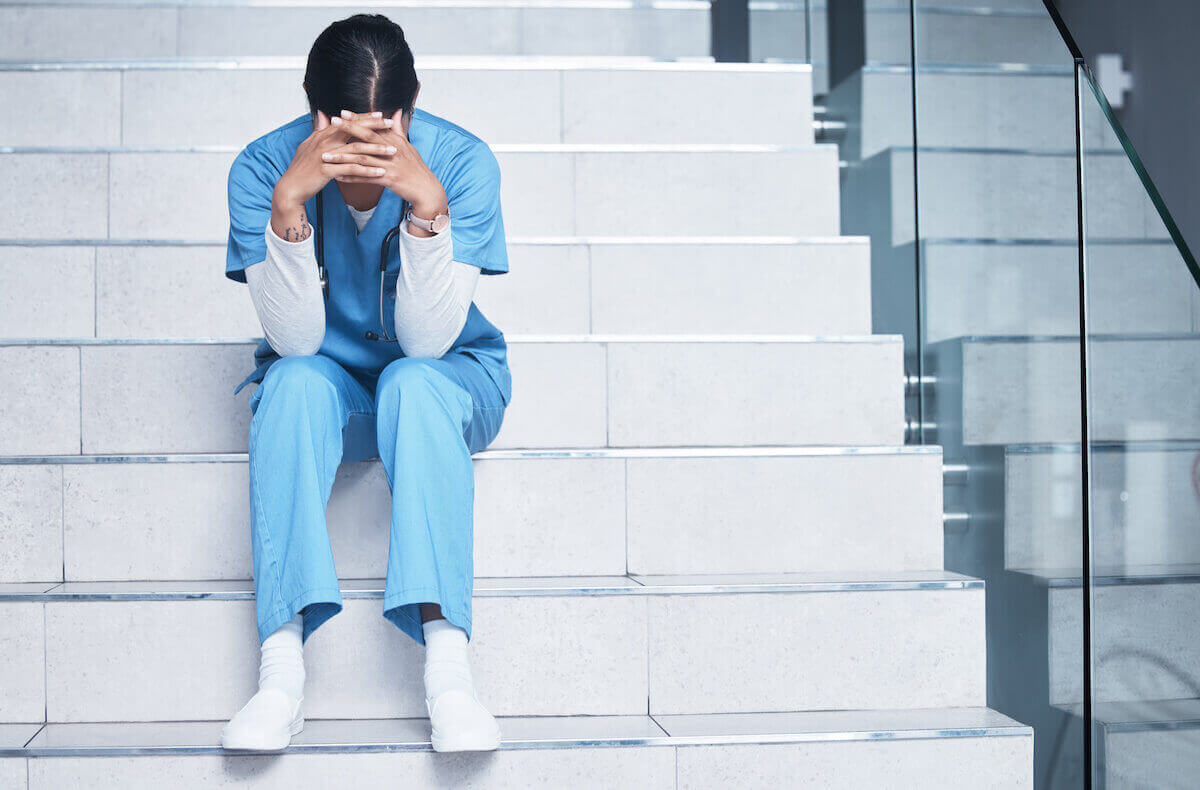 Stressed nurse sitting on steps and hiding face with hands.