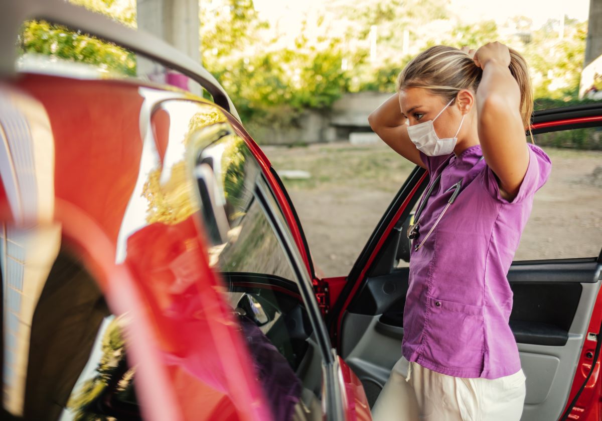 A nurse getting out of her car, fulfilling her duties in accordance with a travel nurse contract.