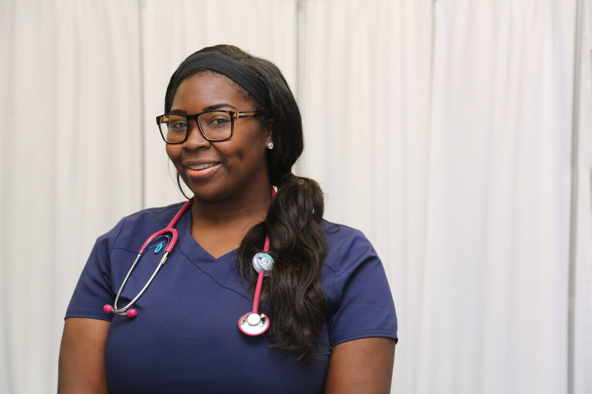 African-American nurse with glasses and wearing navy blue scrubs.