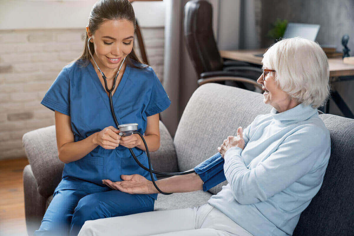 Nurse in scrubs taking blood pressure of a senior woman in her home.