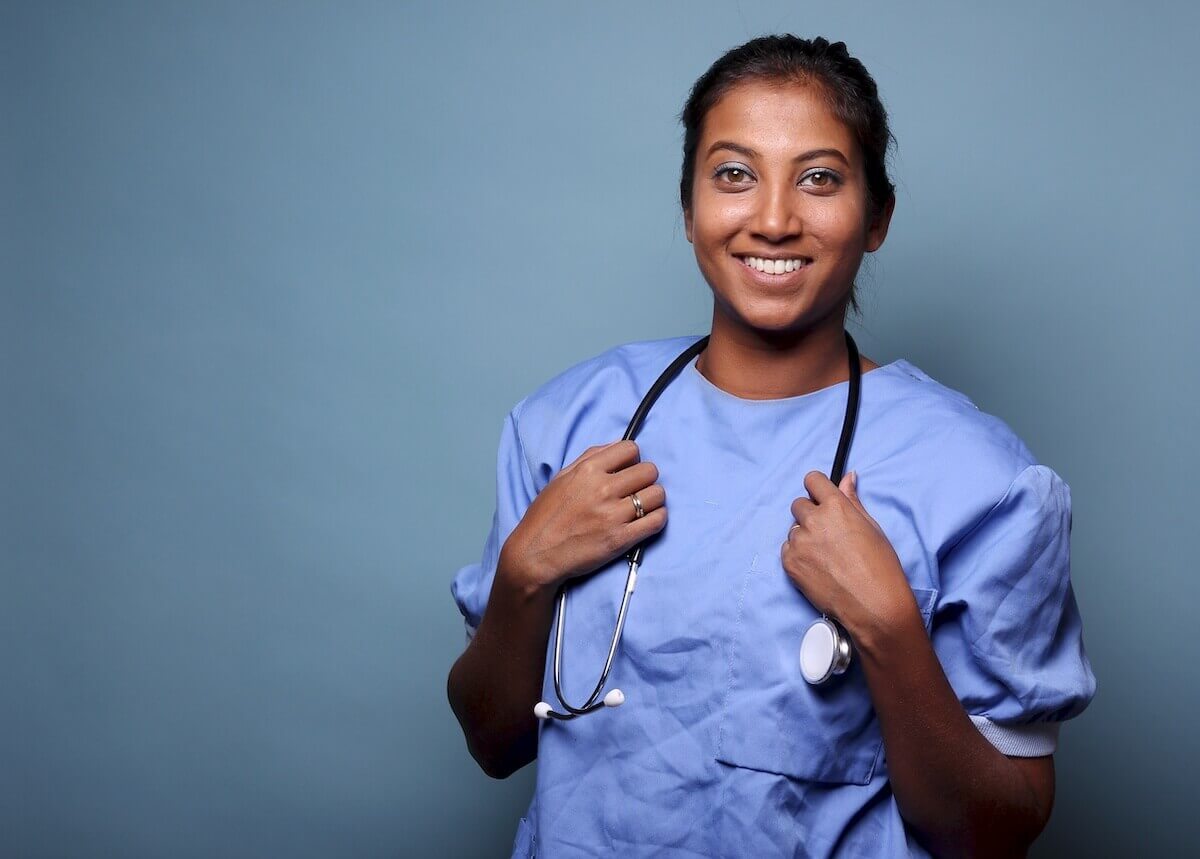 Nurse in scrubs holding stethoscope around her neck and smiling.