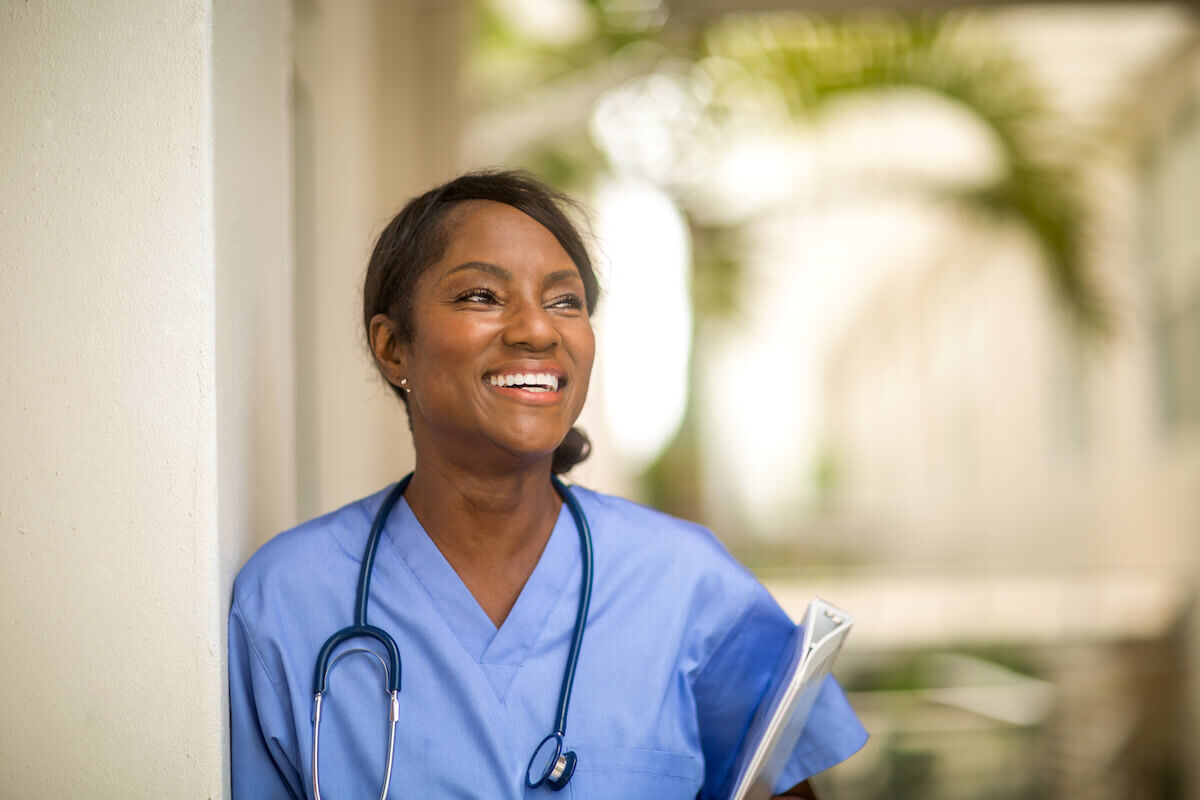 African-American CNA smiling and holding a clipboard outside.