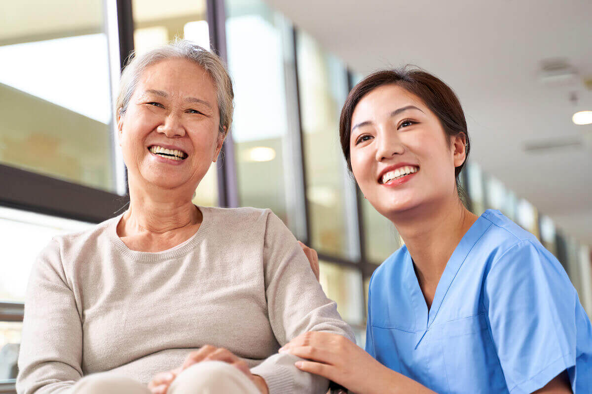 Senior Asian resident smiling with female Asian nurse in long-term care facility.
