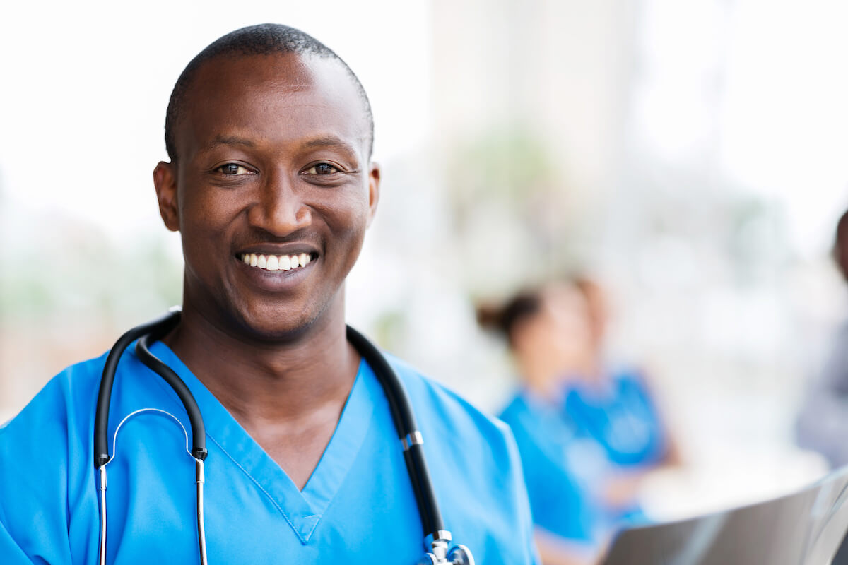 African-American male nurse smiling in blue scrubs.