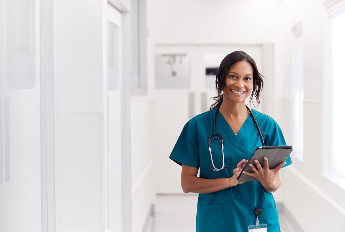 Float pool nurse with tablet smiling in hospital hallway.