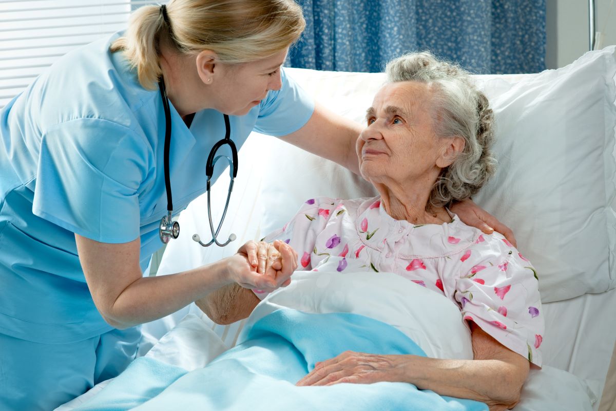 A nurse checks on an elderly patient, holding her hand.