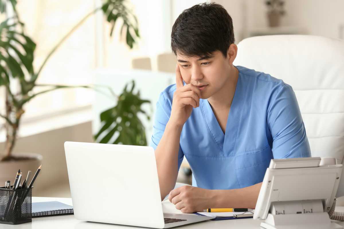 Asian male nurse completing California board of nursing license renewal on computer.