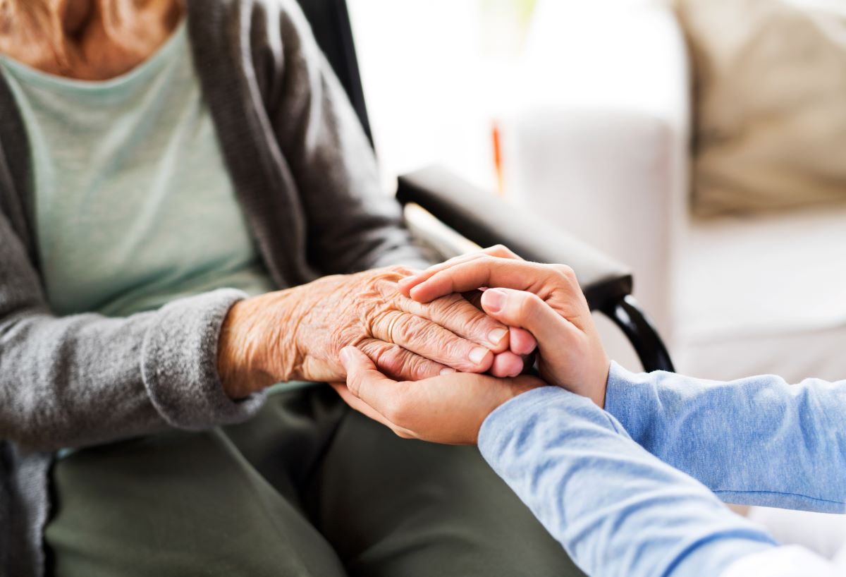 A nurse meeting with a nursing home resident, holds her hand and shows compassion.