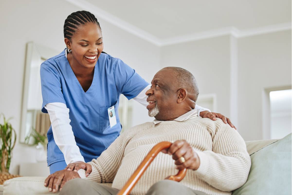 A patient care assistant in blue scrubs greets their patient.