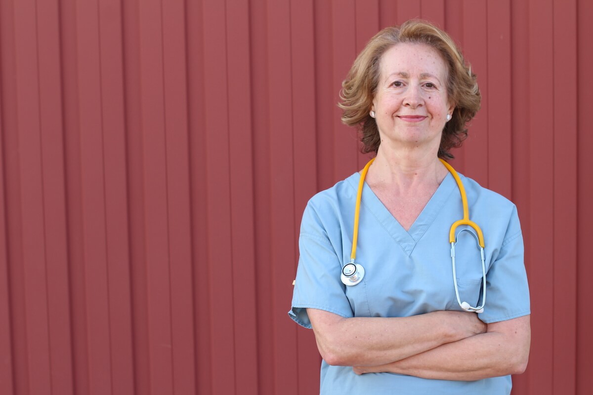 Female travel nurse standing with arms crossed in front of red wall.