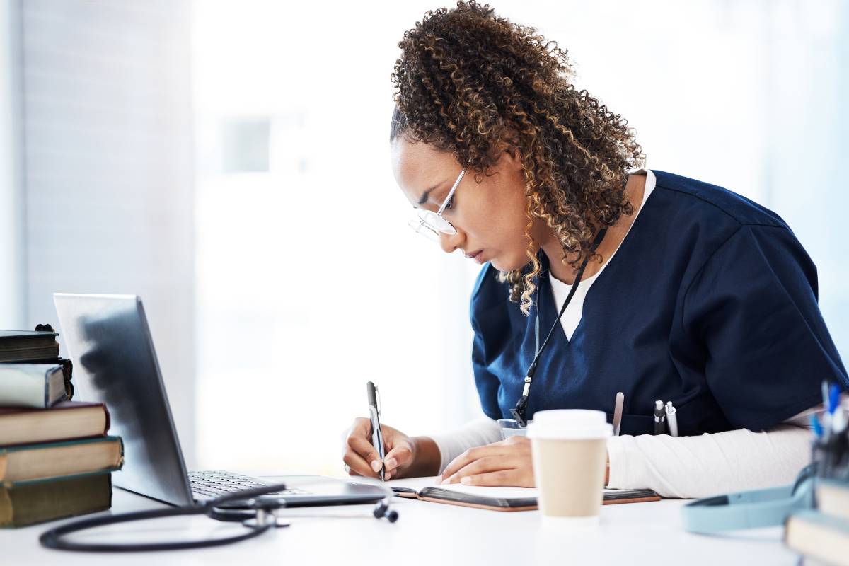 A nurse in blue scrubs writes their NICU nurse resume.