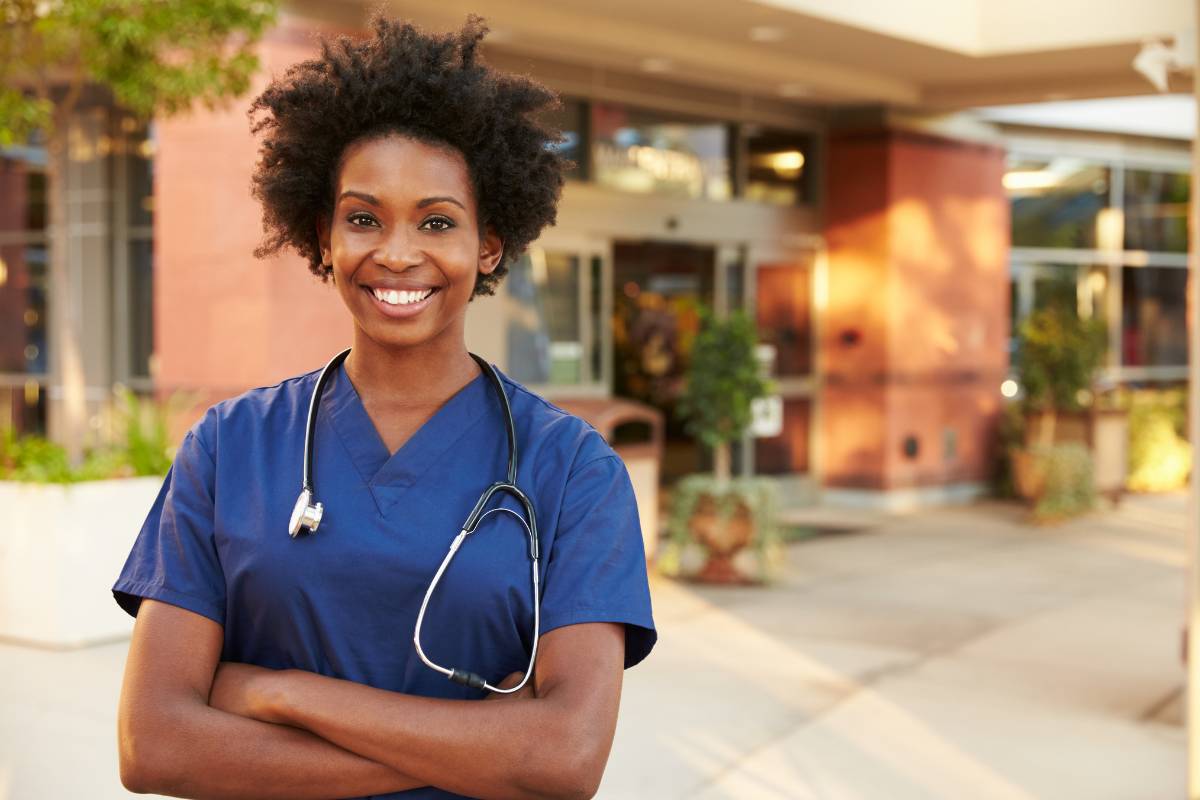 A disney nurse stands outside in blue scrubs.