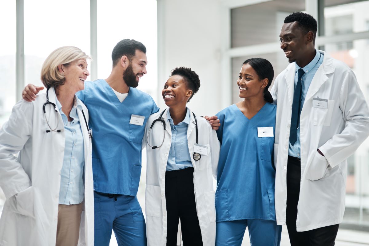 A team of nurses and doctors embrace and smile, showing their appreciation for one another.