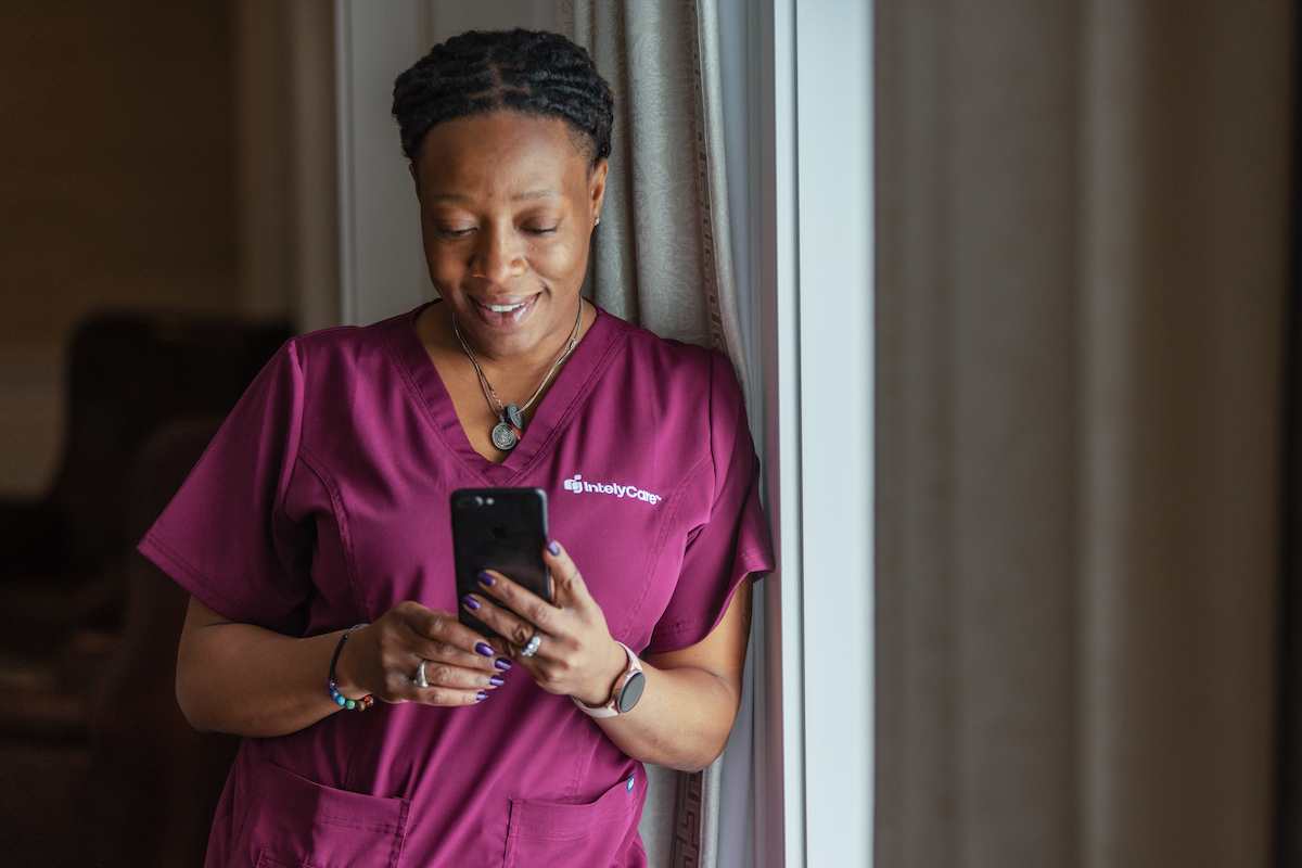 Woman in IntelyCare scrubs looking at her phone for tips on how to be a good agency nurse.