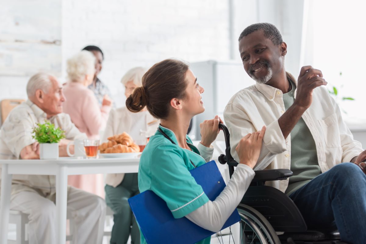 Woman talking to man in a wheelchair in a nursing home