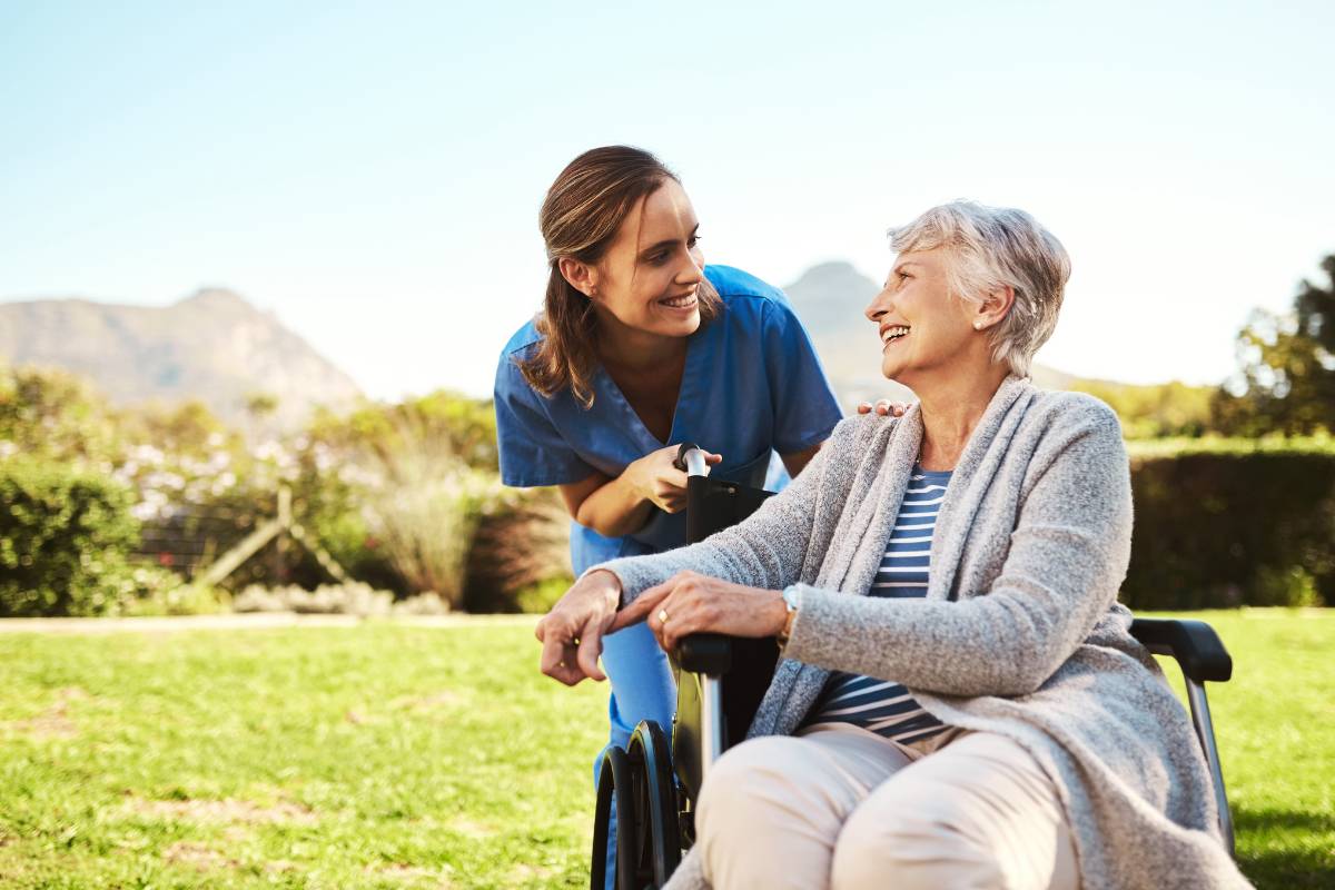 A nurse in blue scrubs smiles at a patient in a rural nursing setting.