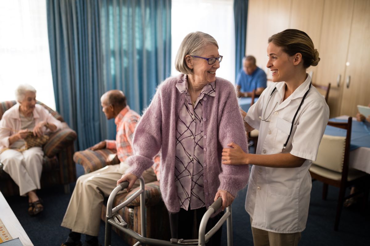 A nurse assists a nursing home resident as she uses a walker for mobility.