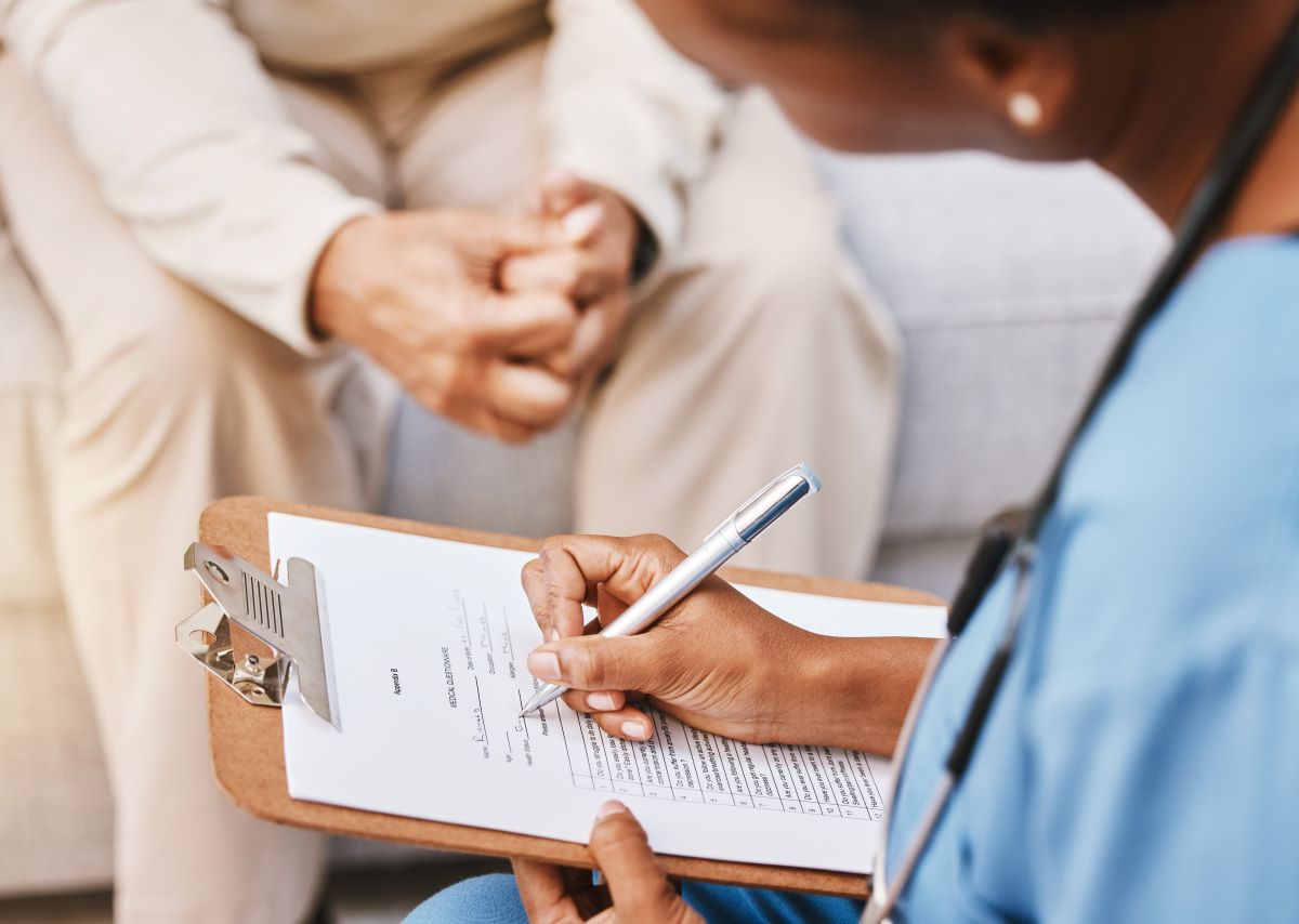 A nurse at a long-term care facility writes down an incident report while interviewing a resident.