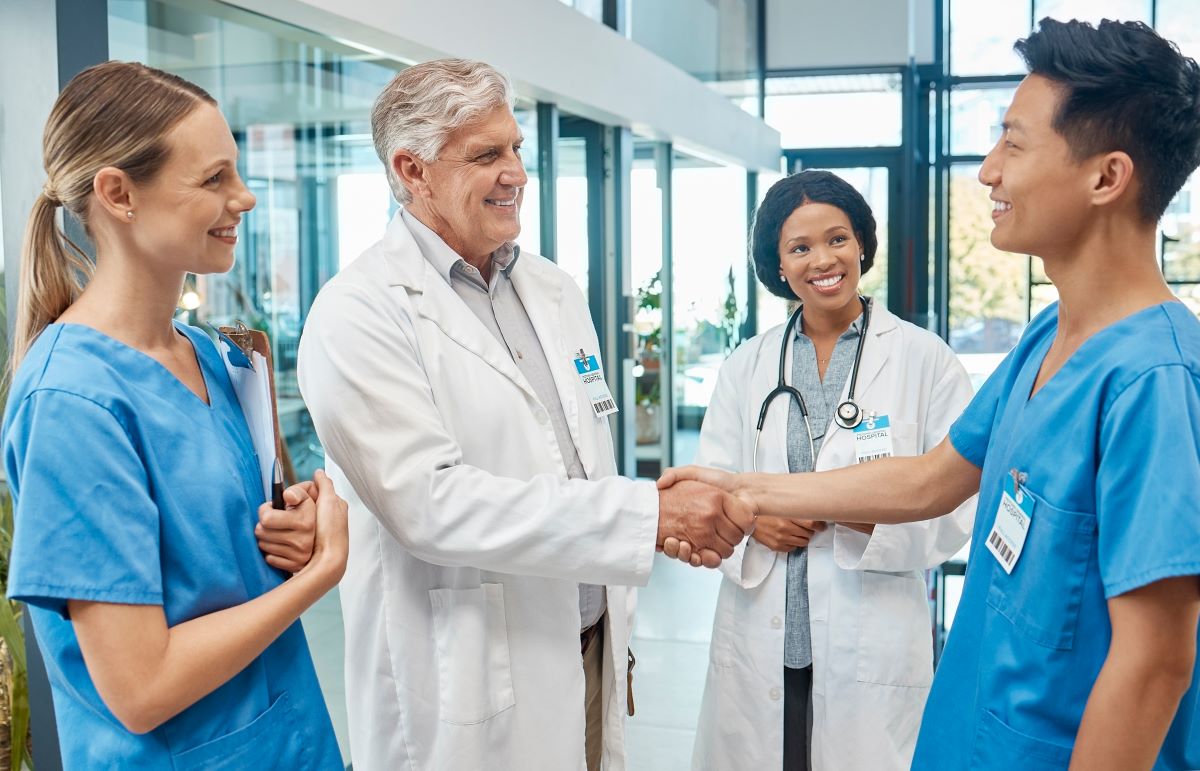 A newly hired nurse meets a fellow nurse and doctor, and shakes hands with a doctor.