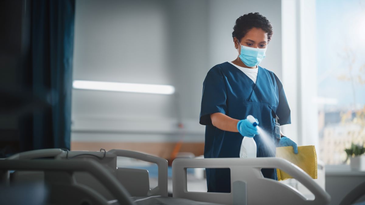 A hospital worker uses an antiseptic spray to clean a hospital bed, one of many standard precautions used to prevent infection.