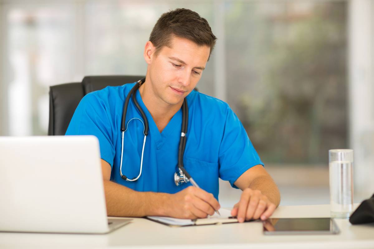 A nurse in blue scrubs writes his STNA resume.