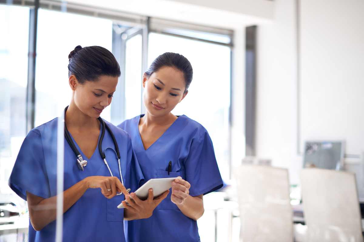 Two nurses looking at a tablet in an office working at a company that hires nurses.