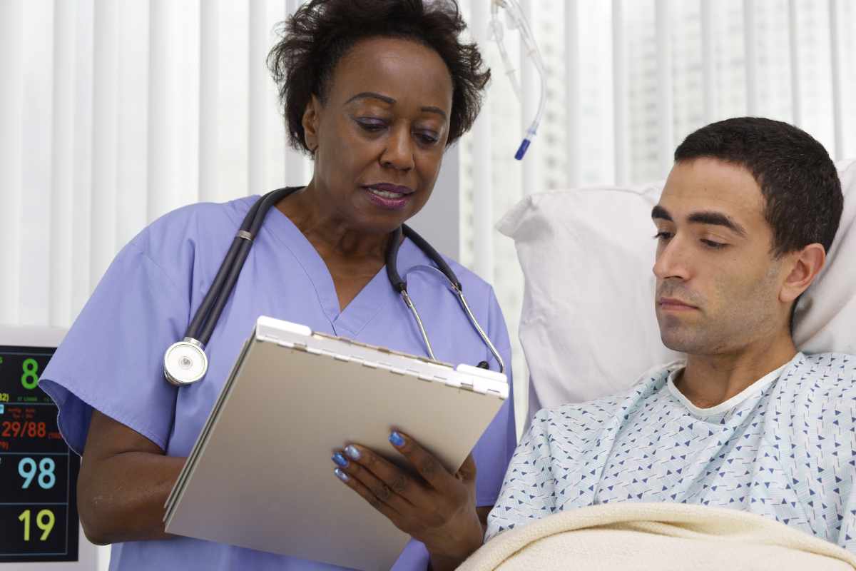 Cardiac nurse reviewing a chart with a patient in a hospital bed.