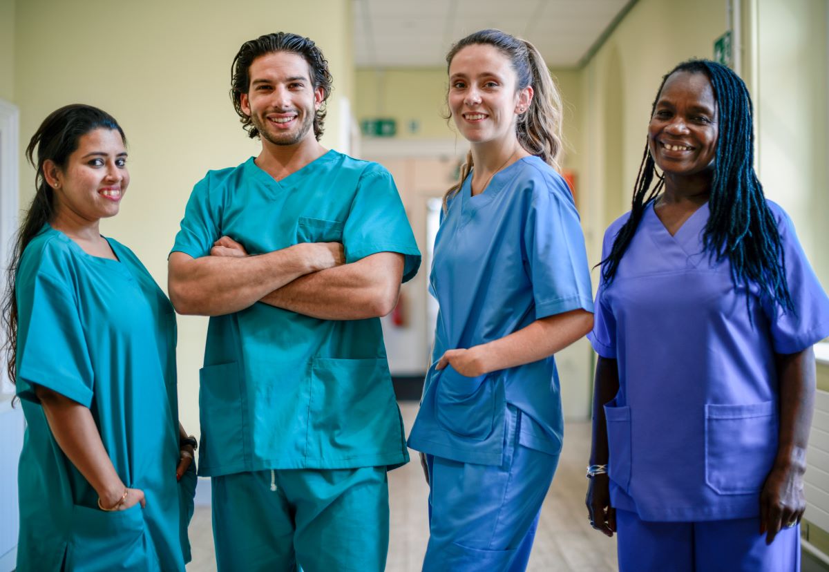 A team of four nurses stands and smiles for the camera.