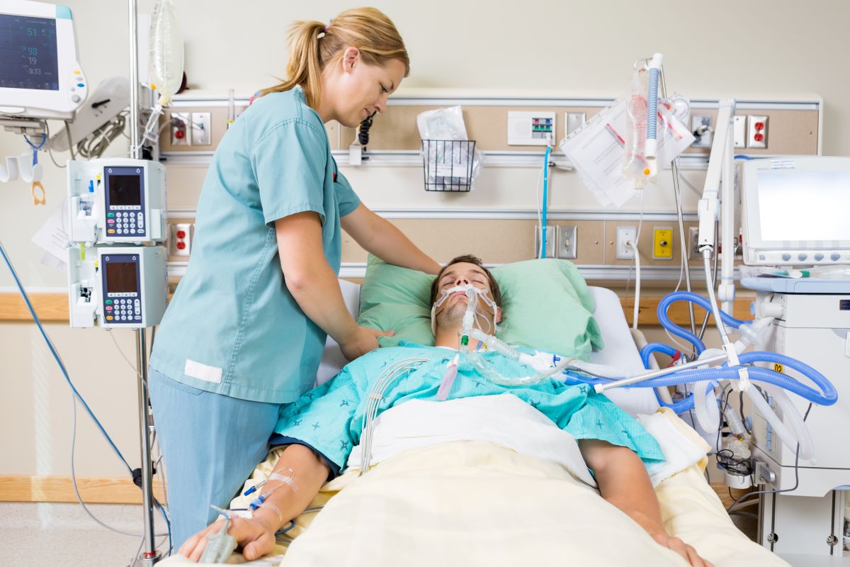 An ICU nurse attends to one of her patients, who is lying in a bed.