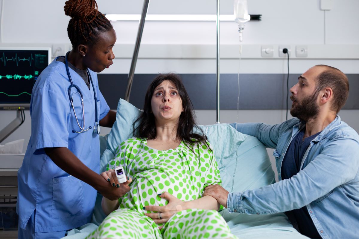 A labor and delivery nurse helps an expectant mother (with her partner near her side) during active labor.
