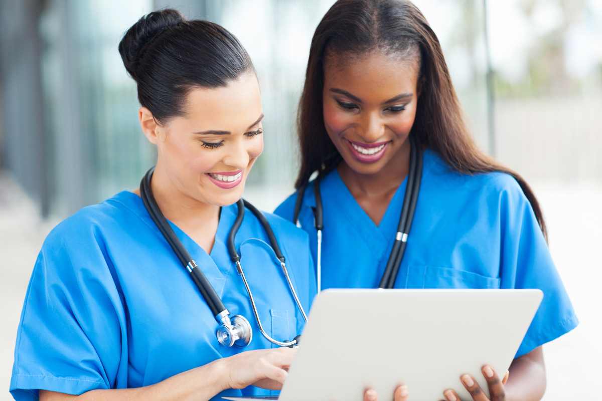 Two nurses reviewing nursing outcomes classification on a laptop