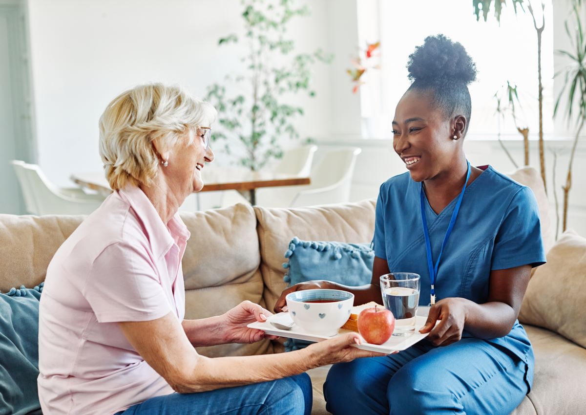 A nurse at a long term care facility serves lunch and spends time with a resident.