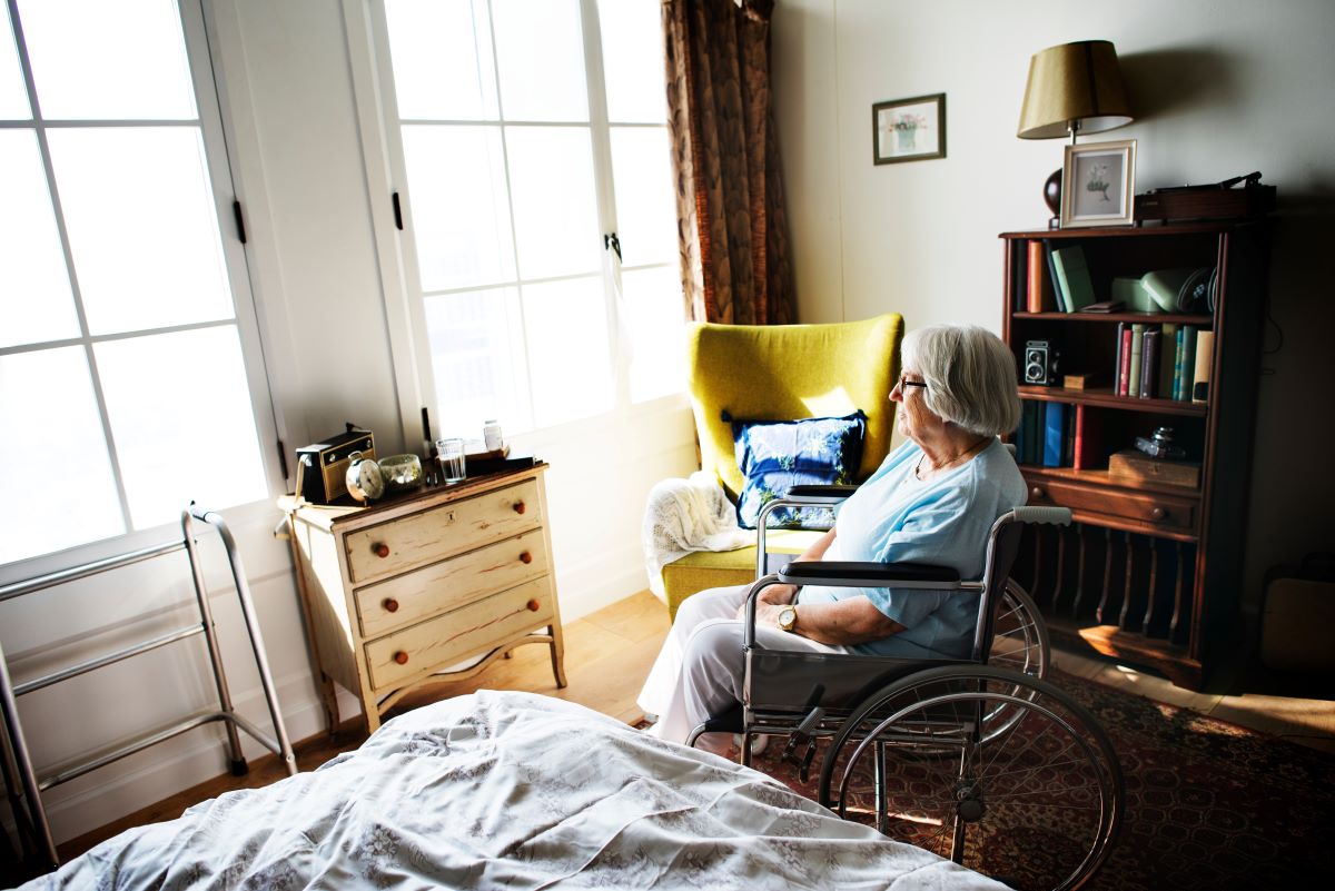 A nursing home resident in a wheelchair gazes out the window.