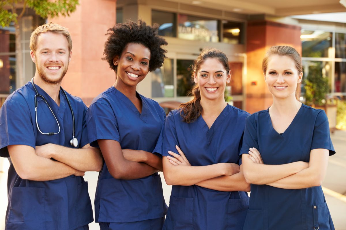 A group of nurses stands with their arms crossed, smiling.