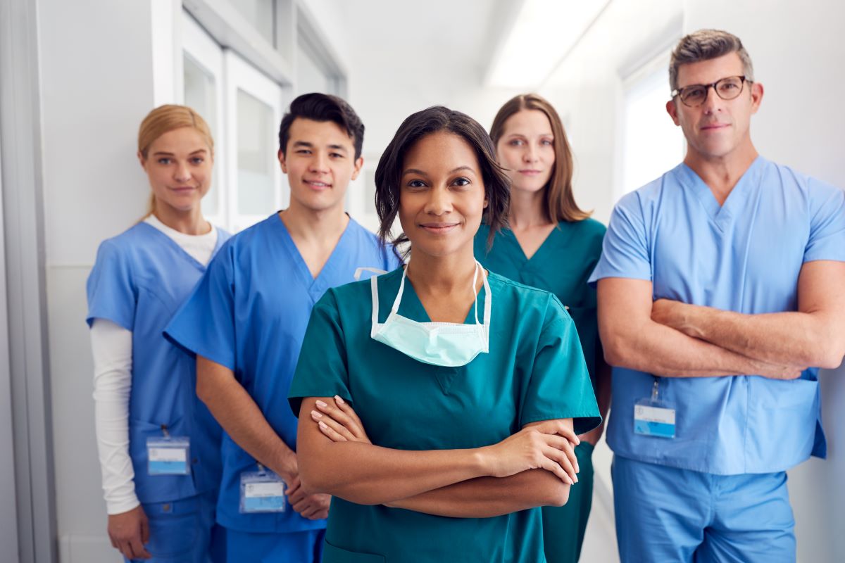 A group of five nurses stands in the hallway of a hospital.