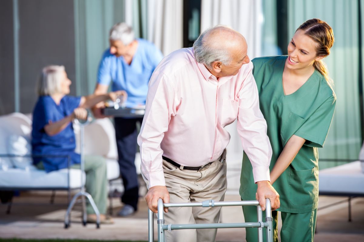 A nurse helps an elderly resident use his walker.