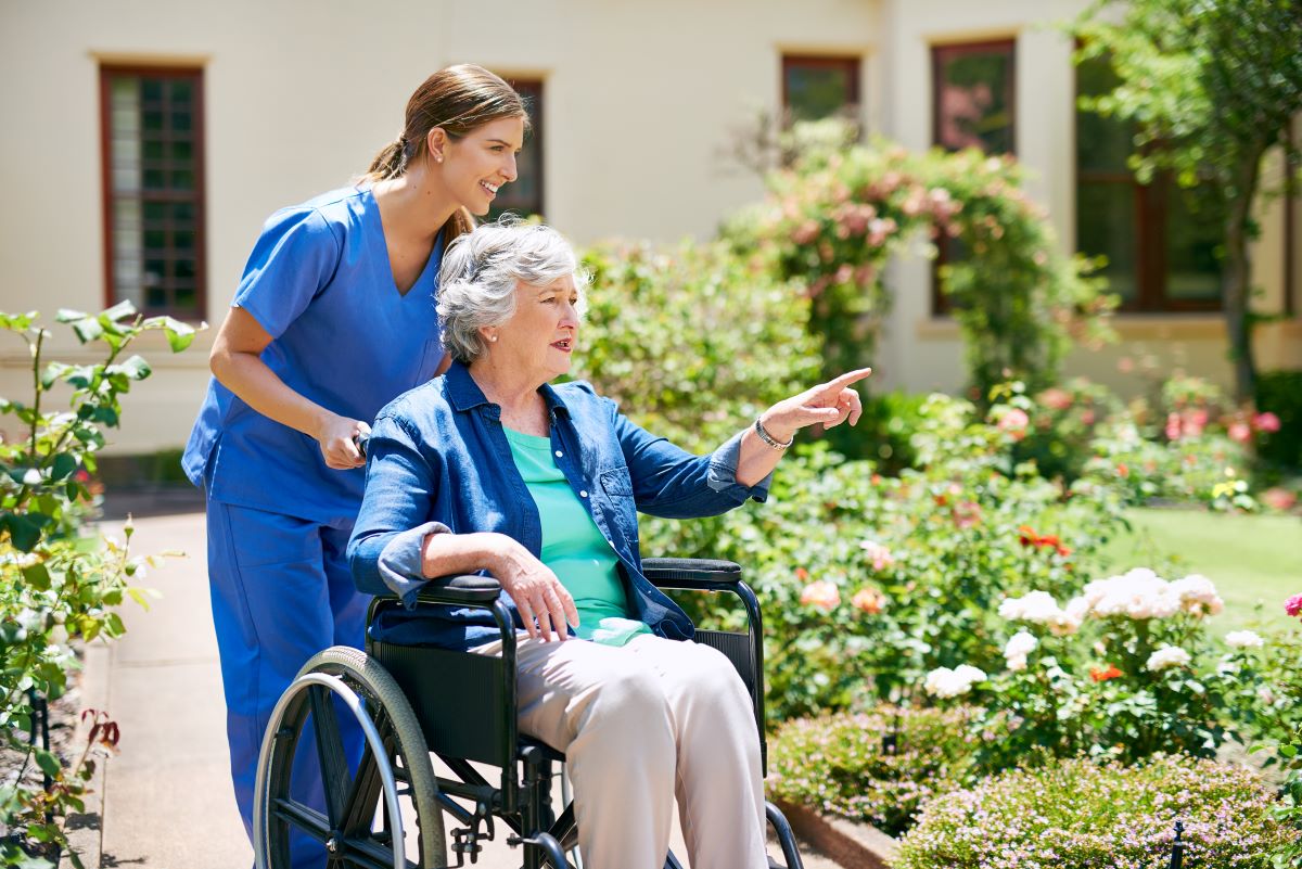 A nurse pushes a resident in a wheelchair around the facility's outside garden area.