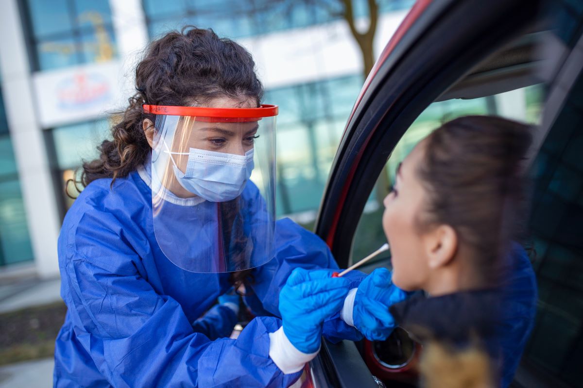 A public health nurse swabs a patient's cheek to determine whether they have a virus at a drive-up clinic.