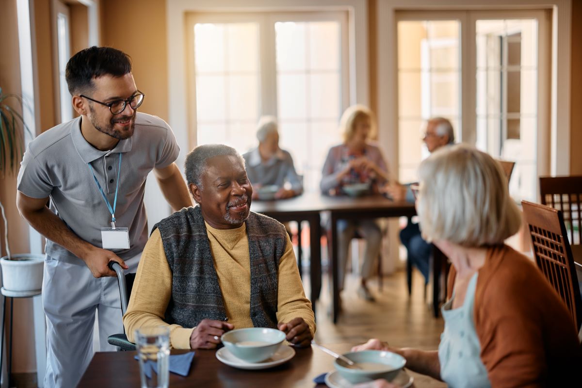 A CNA assists two nursing home residents as they prepare to eat a meal.