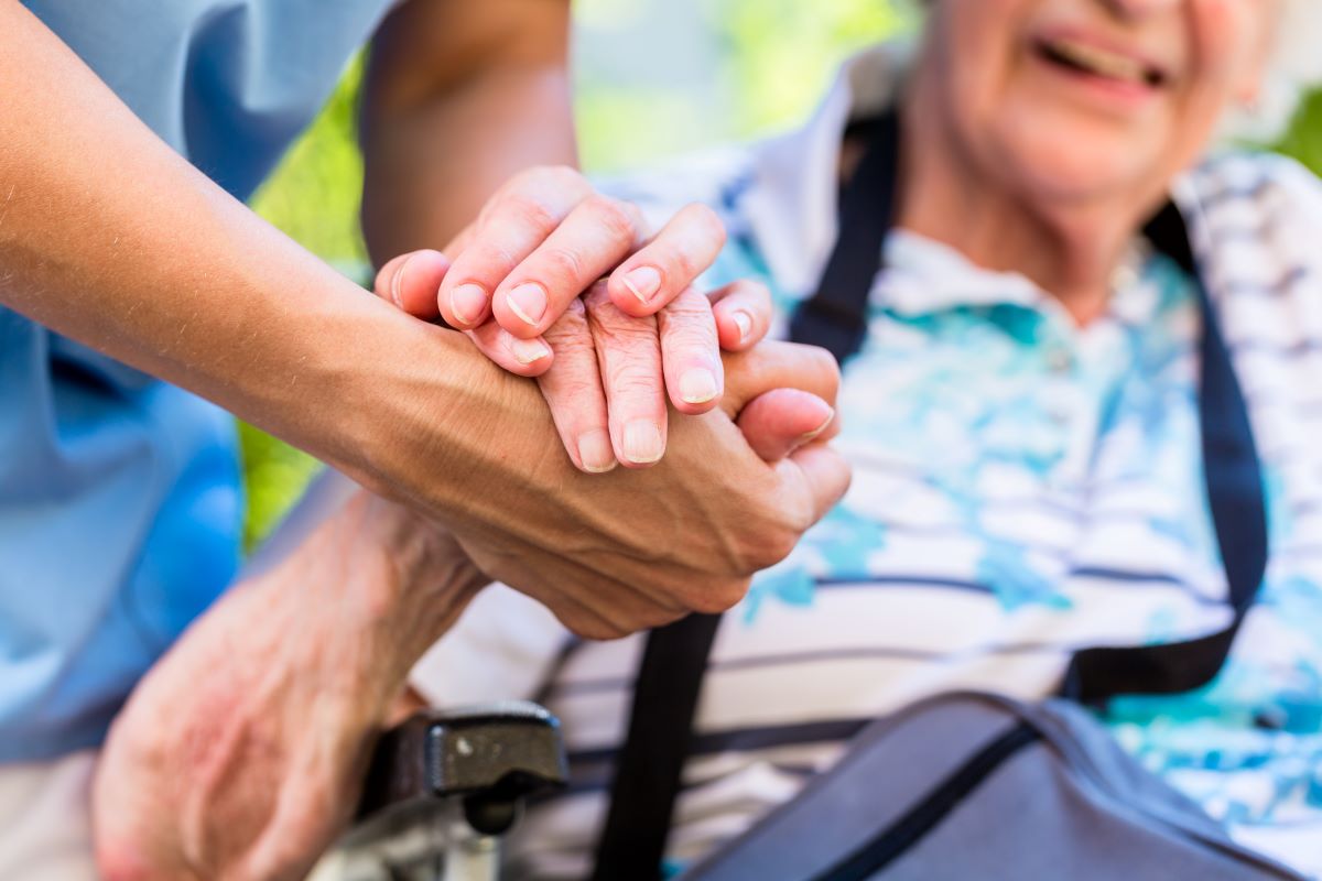 A nurse holds the hand of an elderly nursing home resident.