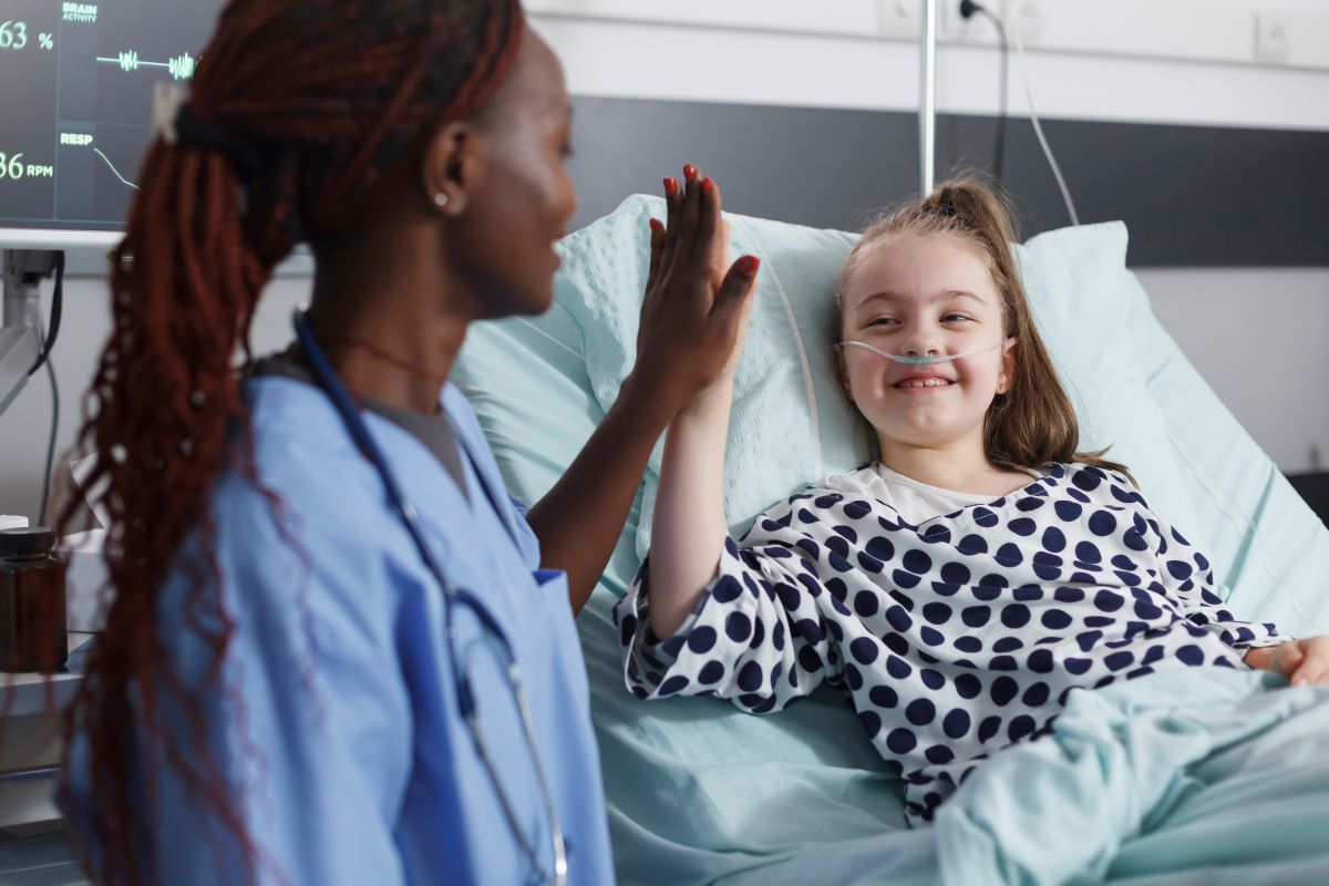 A pediatric nurse high-fives one of her patients, who's lying in a hospital bed.