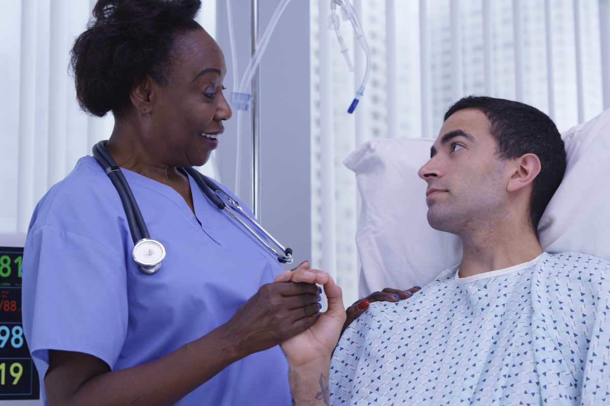 African-American nurse holding bedridden patient's hand and exhibiting the use of soft skills in nursing.