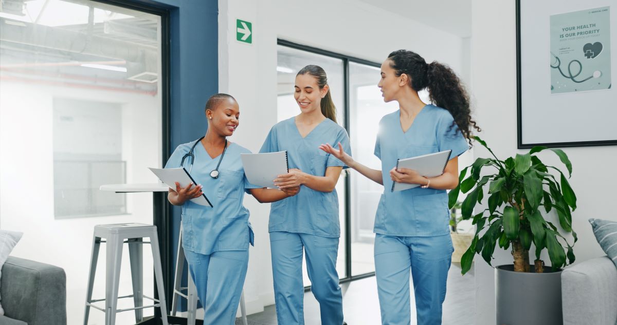 Three nurses walk down a facility hall together.