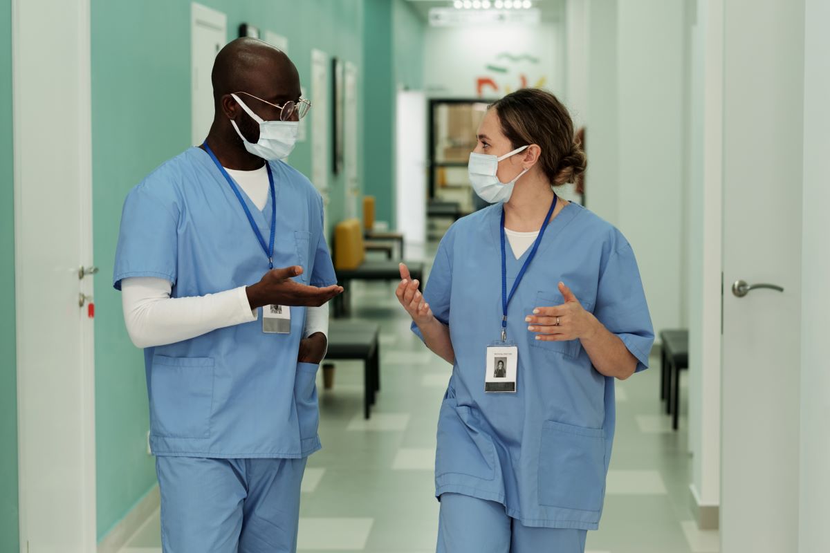 Two nurses having a discussion as they walk down a facility's hallway.